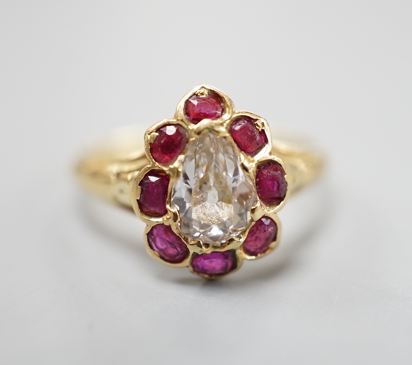 An early 20th century yellow metal and pear cut single stone diamond ring, with ruby set border, size O, gross weight 3.3 grams.